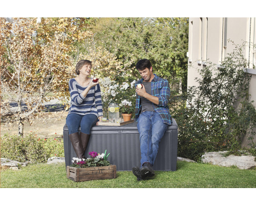 Scéna s úložným boxem v zahradě, na kterém sedí pár a vychutnává si nápoje