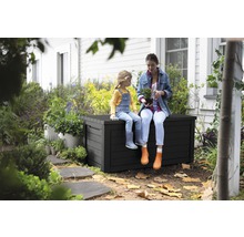 Žena a dítě sedí na černé zahradní bedně v zahradě.