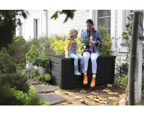 Žena a dítě sedí na černé zahradní bedně v zahradě.