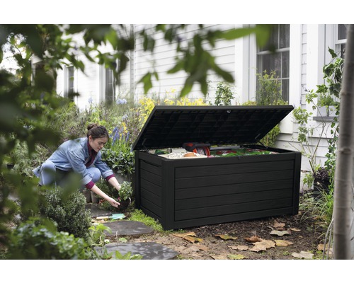 Zahradní scéna s ženou klečící vedle otevřeného, černého zahradního boxu