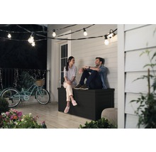 Pár sedí na černé zahradní bedně na terase pod světelným řetězem.