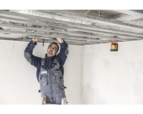 Muž montuje stropní konstrukci s laserovou vodováhou v místnosti.