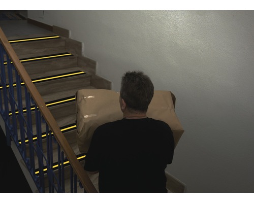 Muž nese balík po schodech s protiskluzovými proužky