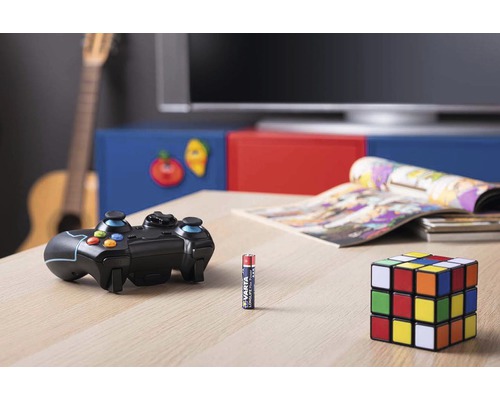 Hrací scéna s herním ovladačem, baterií a Rubikovou kostkou na stole