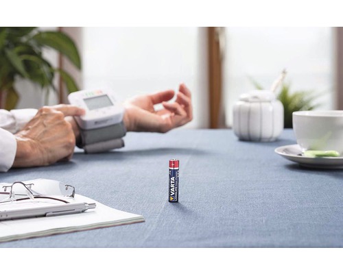 Scéna s tonometrem na zápěstí osoby a jednou baterií Varta Micro na stole