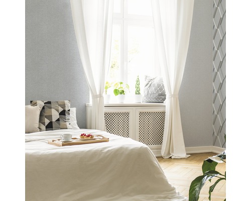 Světlá ložnice s postelí, závěsy a stěnou se strukturovanou tapetou