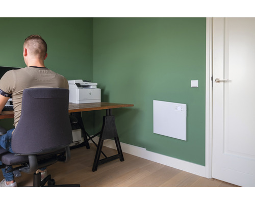 Kancelář s topným panelem na zdi, psacím stolem a kancelářskou židlí.