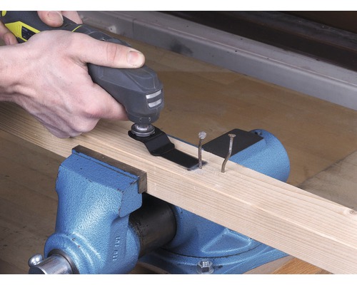 Osoba používá multifunkční nástroj k řezání hřebíků v dřevěné desce, která je upevněna ve svěráku.