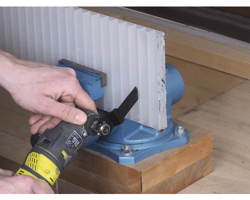 Průhledná komůrková deska je upnutá ve svěráku a je řezaná multifunkčním nástrojem.