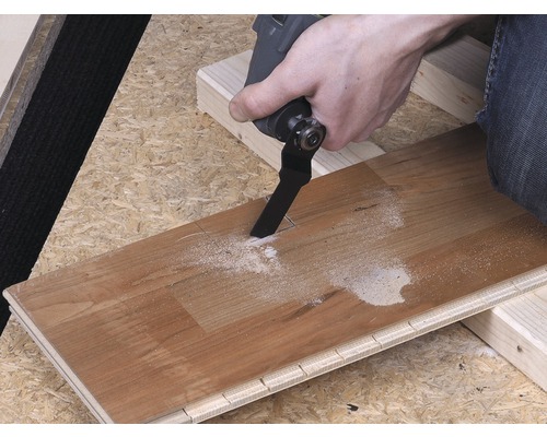 Osoba řeže dřevěnou desku pomocí multifunkčního nástroje.