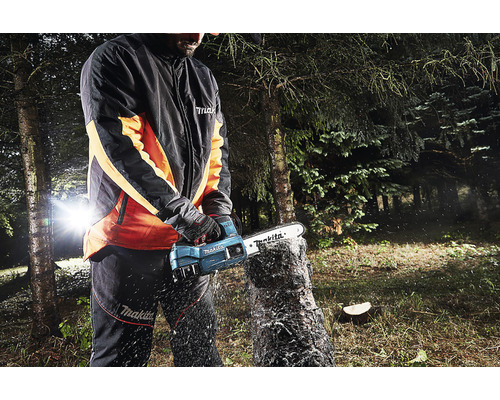 Osoba používá akumulátorovou řetězovou pilu Makita k řezání kmene stromu venku.