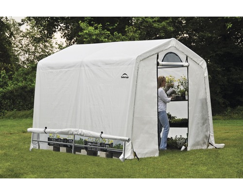 Skleník s policemi a ženou zalévající rostliny