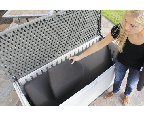 Žena ukládá polštáře do šedobílé zahradní truhly.