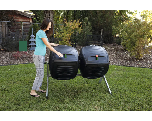 Dva kompostéry bubnové s ženou otevírající jeden z bubnů na zahradě.