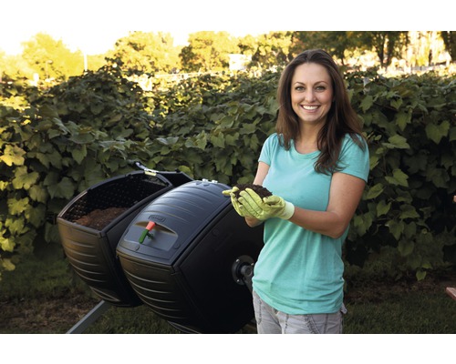 Žena drží zeminu před otočným kompostérem na zahradě.