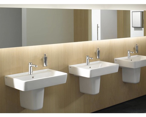 Tři bílá umyvadla s vodovodními bateriemi a dávkovači mýdla v koupelně.