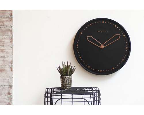 Nástěnné hodiny s logem Nextime, pokojová rostlina na stole