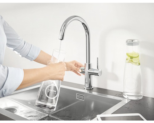 Žena plní sklenici vodou z baterie Grohe Blue v umyvadle.