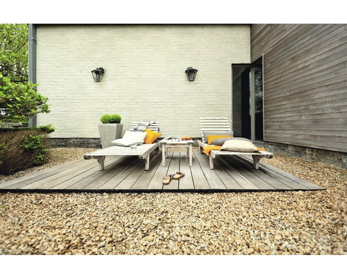 Terasa se dvěma lehátky, malým stolem a ozdobnými polštáři na štěrku