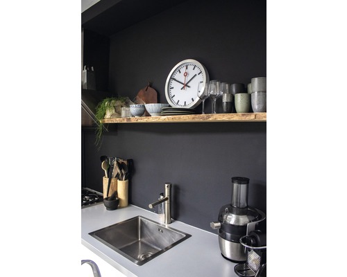 Kuchyňská scéna s dřezem, baterií, kuchyňským náčiním, odšťavňovačem a nástěnnou policí s hodinami, nádobím a dekoracemi