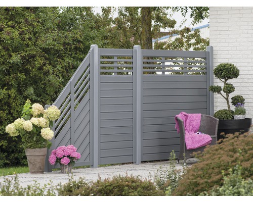 Zahradní scéna s šedým soukromým plotem, rostlinami a posezením