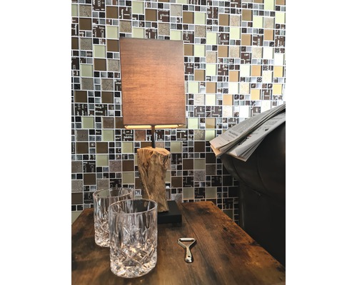 Dekorativní stůl s lampou, dvě sklenice a otvírák na láhve před mozaikovou stěnou