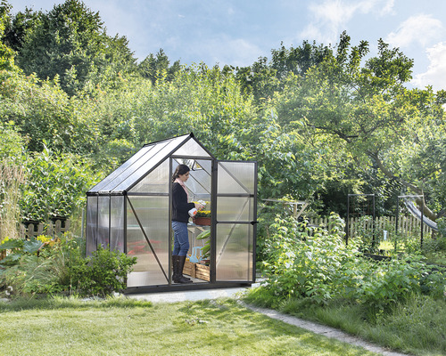 Skleník s otevřenými dveřmi a osobou pečující o rostlinu na zahradě