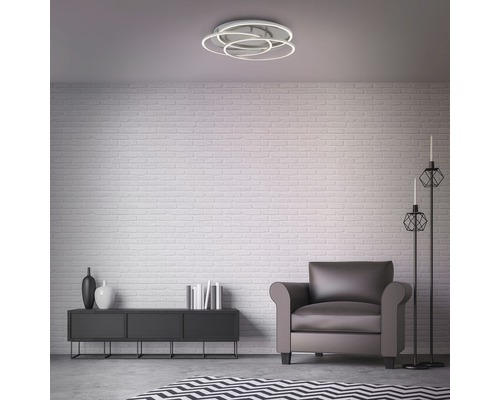 Obývací pokoj se stropním svítidlem, křeslem a dekorací na příborníku před cihlovou zdí