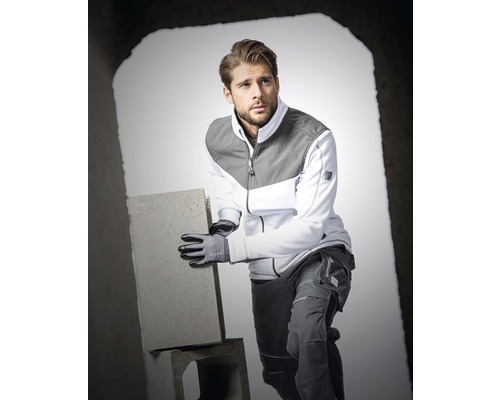 Muž má na sobě pracovní oděv a rukavice a drží cihlu