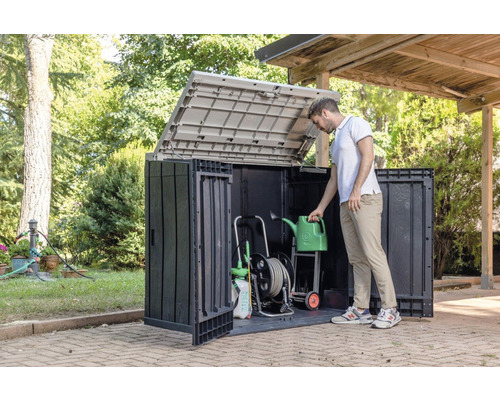 Zahradní skříň s otevřeným víkem a zahradním nářadím a osobou držící konev