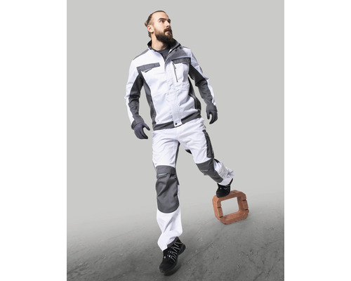 Muž v pracovním oděvu s bundou a kalhotami stojící na cihle