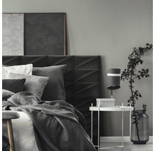 Ložnice s postelí, nočním stolkem a dekorací v šedých tónech.