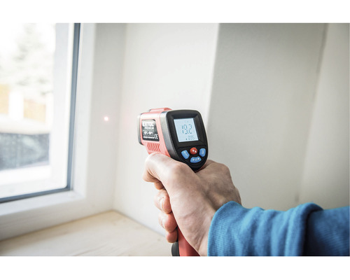 Ruka drží infračervený teploměr pro měření teploty okna