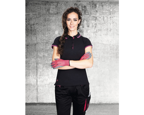 Žena s pracovními rukavicemi, pracovní polokošilí a pracovními kalhotami před betonovou stěnou