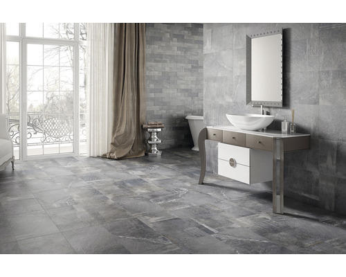 Moderní koupelna s šedými obklady stěn a podlah, umyvadlovou skříňkou, zrcadlem a vanou.