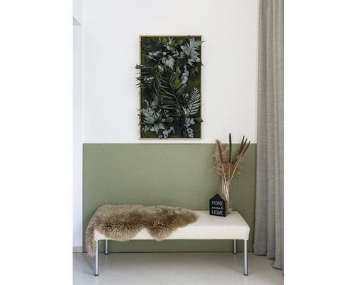 Dekorativní mechový obraz s různými druhy rostlin, včetně kapradin a eukalyptu, na stěně nad lavicí s ovčí kůží