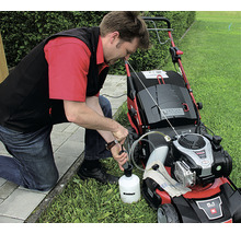 Muž doplňuje olej do sekačky na trávu