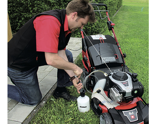 Muž doplňuje olej do sekačky na trávu