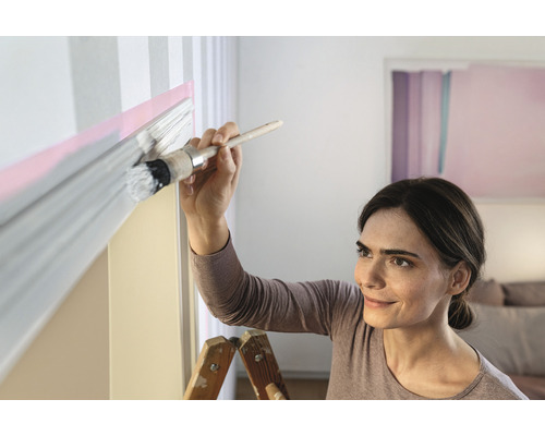 Žena maluje stěnu štětcem a barvou.