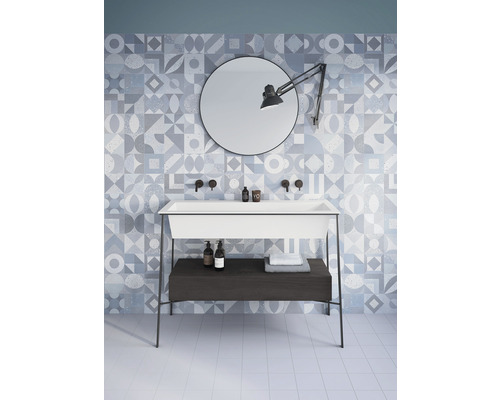 Světlá koupelna se vzorovanými obklady, umyvadlo se skříňkou, zrcadlo a lampa.