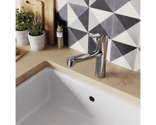 Kuchyňská vodovodní baterie z kovu na dřezu s pozadím vzorovaných dlaždic