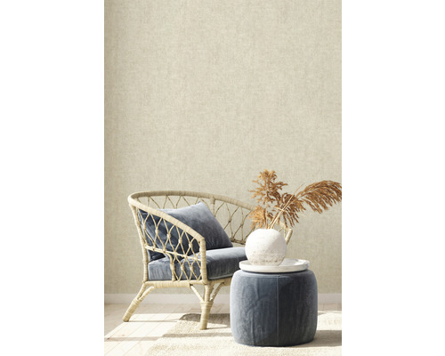 Dekorativní interiér s ratanovým křeslem, polštářem a odkládacím stolkem před béžovou tapetou.