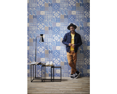 Scéna s nástěnnou tapetou v patchworkovém designu, sadou příručních stolků a stojací lampou.