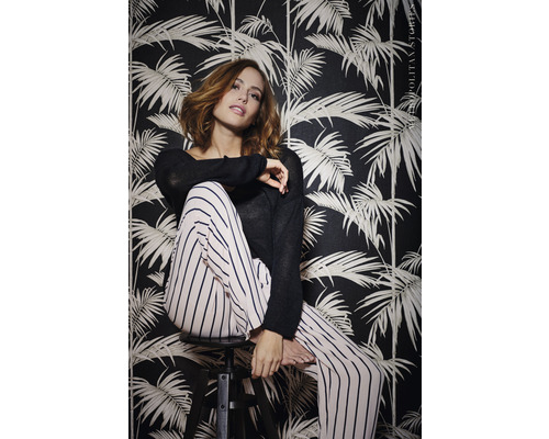 Žena sedí před tmavou tapetou s rostlinnými motivy