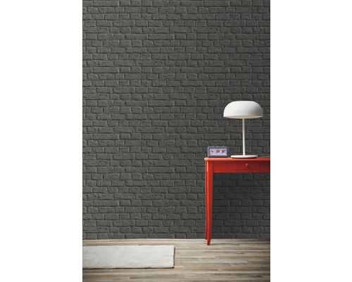 Pokoj s šedou cihlovou zdí, červeným stolem a lampou.