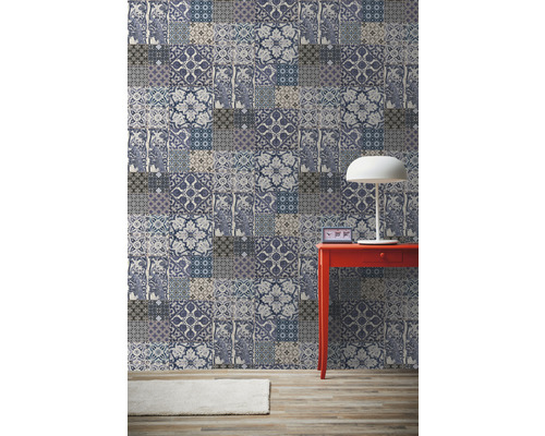 Pohled do místnosti s patchworkovou tapetou, červeným stolem a lampou