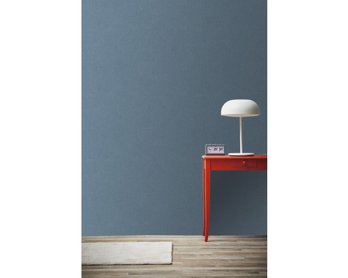 Světle zbarvený koberec, modré pozadí, červený stůl s hodinami a lampou