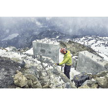 Pracovník v ochranném oděvu pracuje na staveništi v horách s kufříkem na nářadí od společnosti Dewalt.