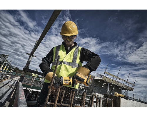 Stavební dělník s ochrannou helmou a vestou pracující s úhlovou bruskou na řezání armovacích tyčí na staveništi