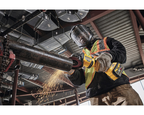 Muž brousí trubku akumulátorovou úhlovou bruskou DeWalt Flexvolt.